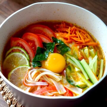 Tom Yum Noodles in a pot with tomato, cucumber, limes & surimi