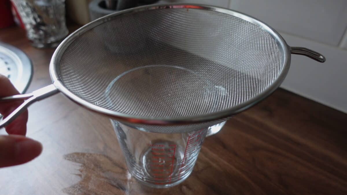 Straining pandan juice through a fine mesh sieve into a glass jar