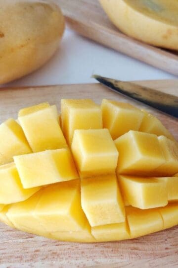 Freshly cut mango cubes on a wooden cutting board with whole mangoes in the background.