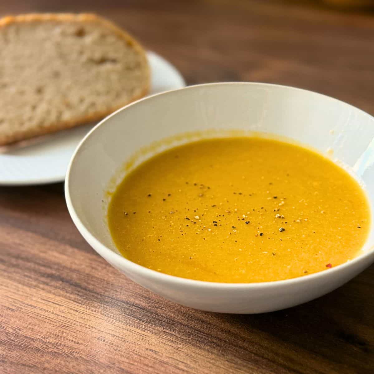 Butternut squash & red lentils soup in a white bowl,served with bread